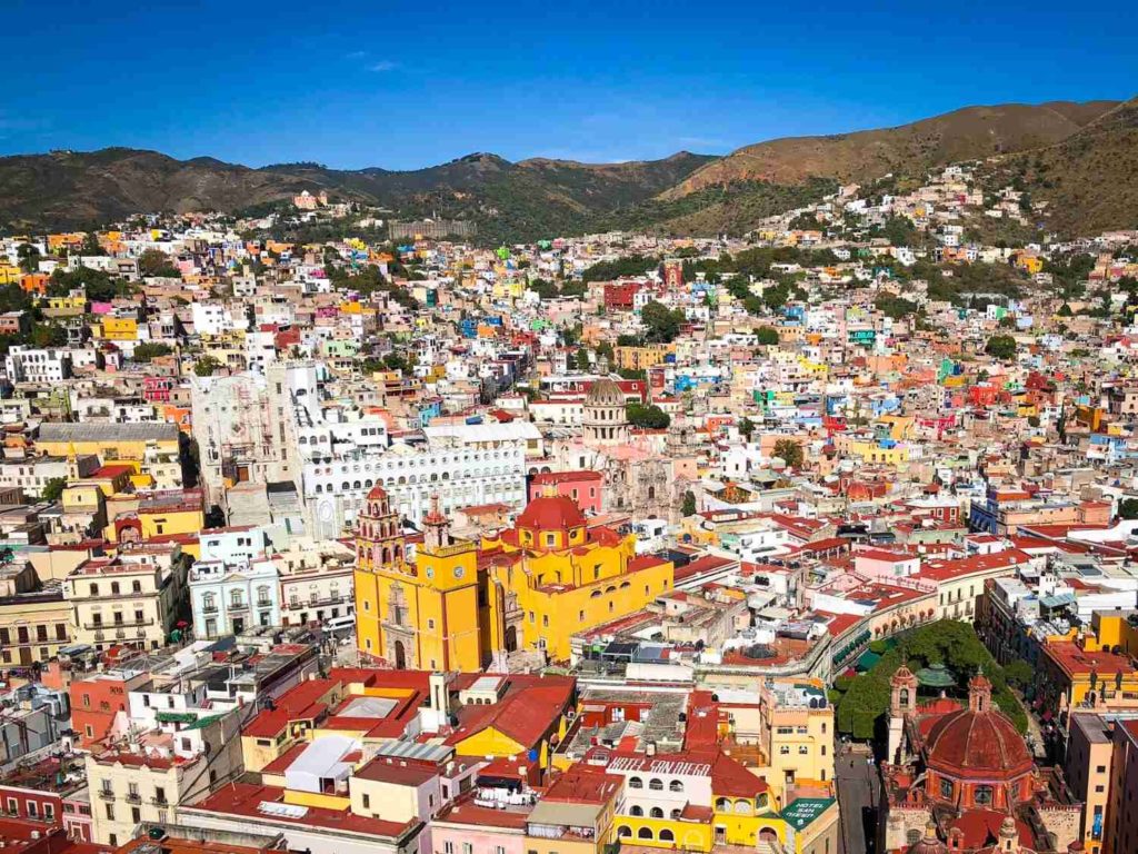 An aerial view of Guanajuato City with Parroquia de Santa Fe de Guanajuato in the center, surrounded by colorful buildings and the hills