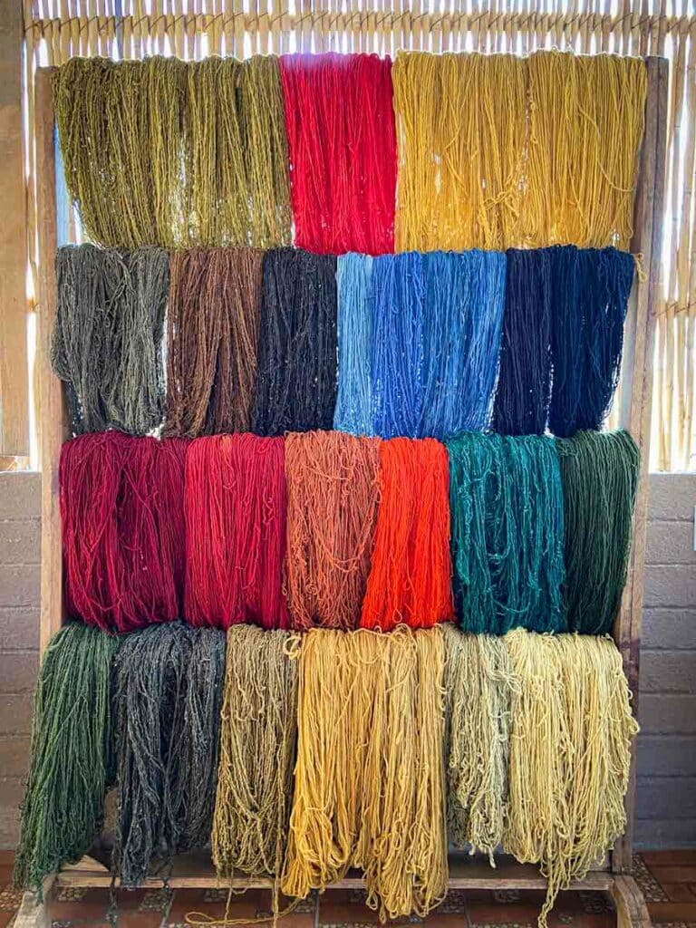 Rack of colorful wool yarn with four levels of wool of various colors hanging from it.
