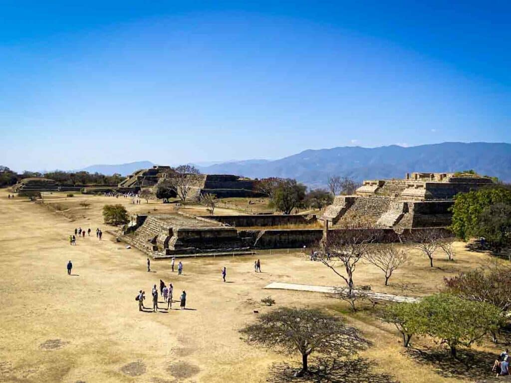 View of Monte Alban archeological site consisting of two pyramid structures backed by a mountain range.