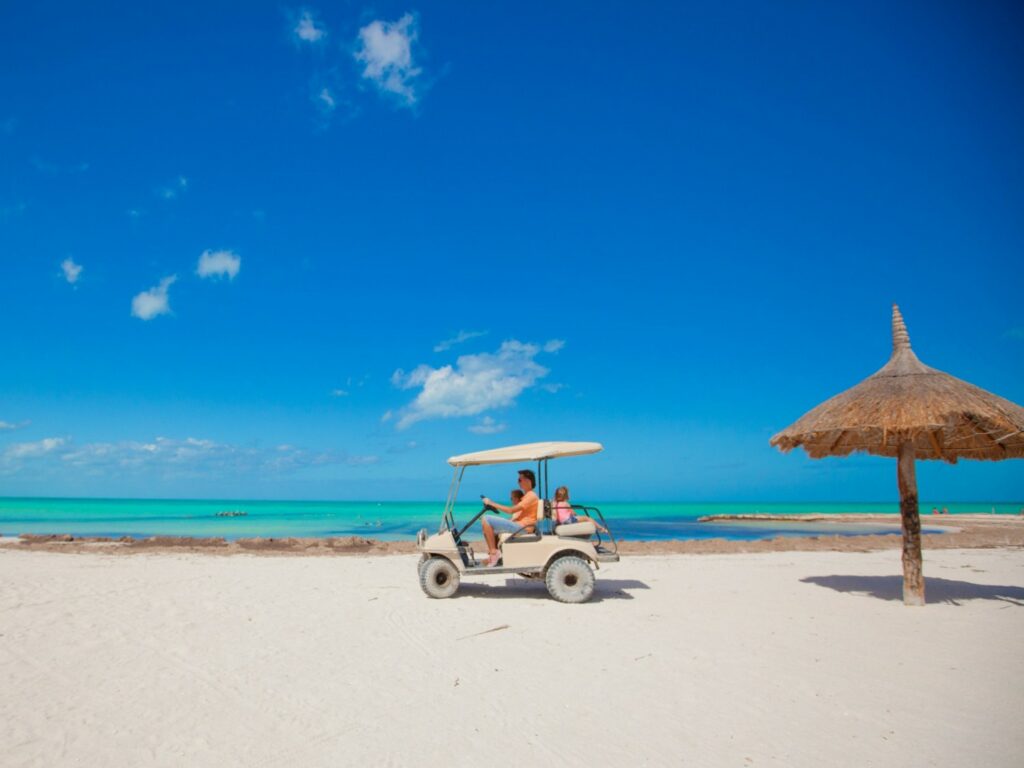 Man and two girls riding in a golf cart on a beach